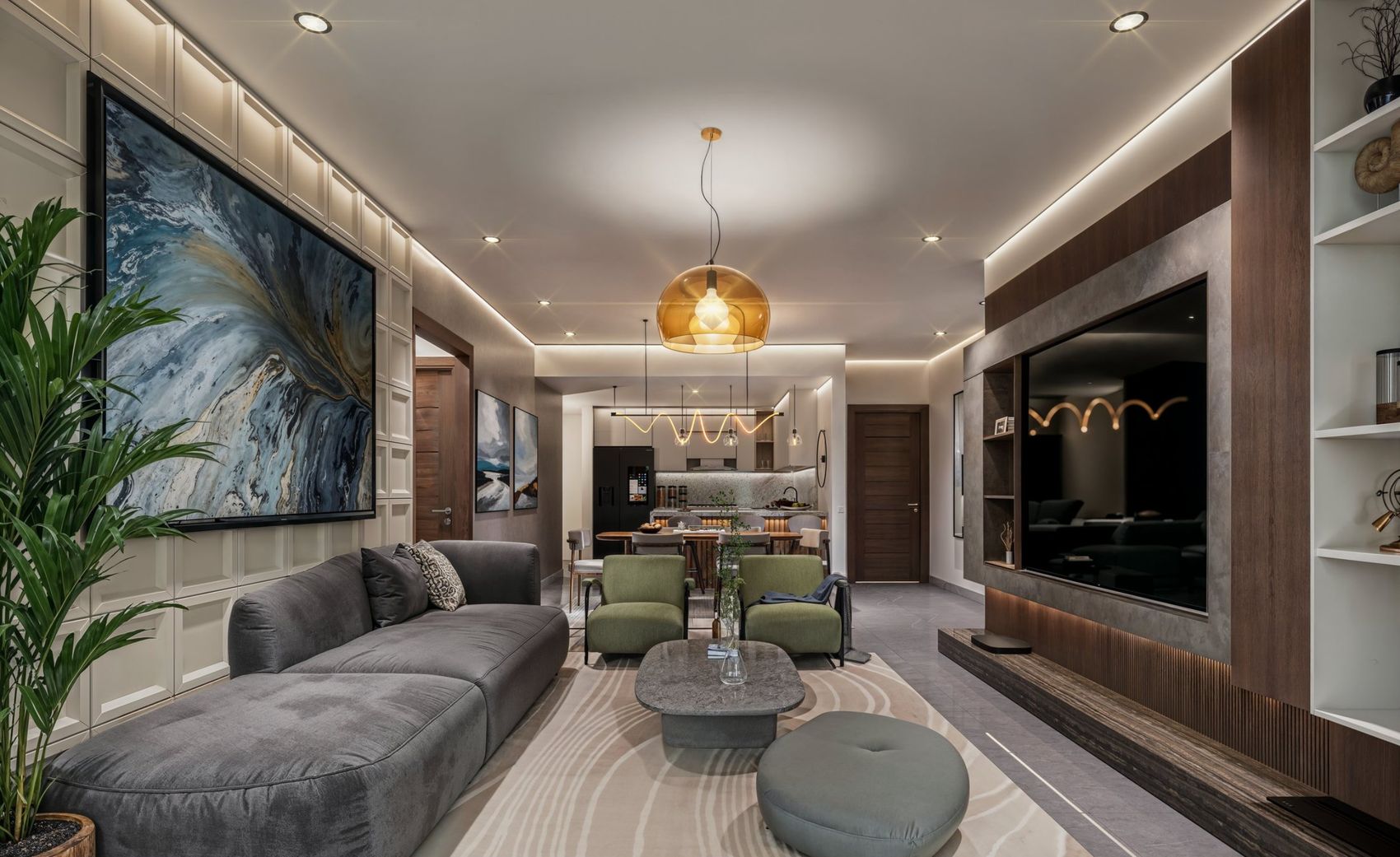 Sala con sofá gris, mesa de centro y pared de TV en madera, con el comedor y la cocina al fondo